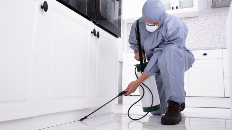 a person in a protective suit spraying a white cabinet to prevent cockroach in the house